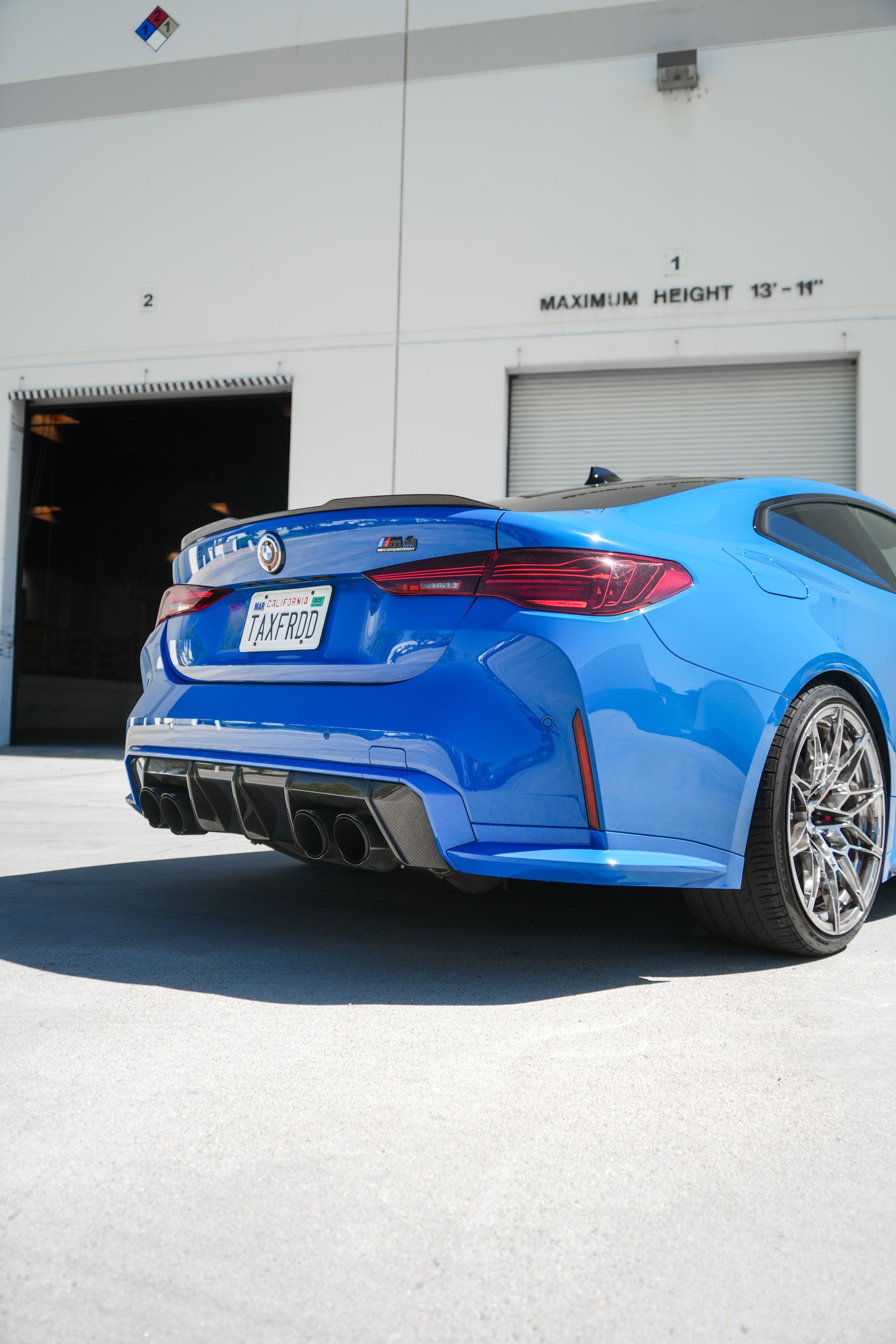 Blue sports sedan parked outside a garage with custom wheels and rear diffuser