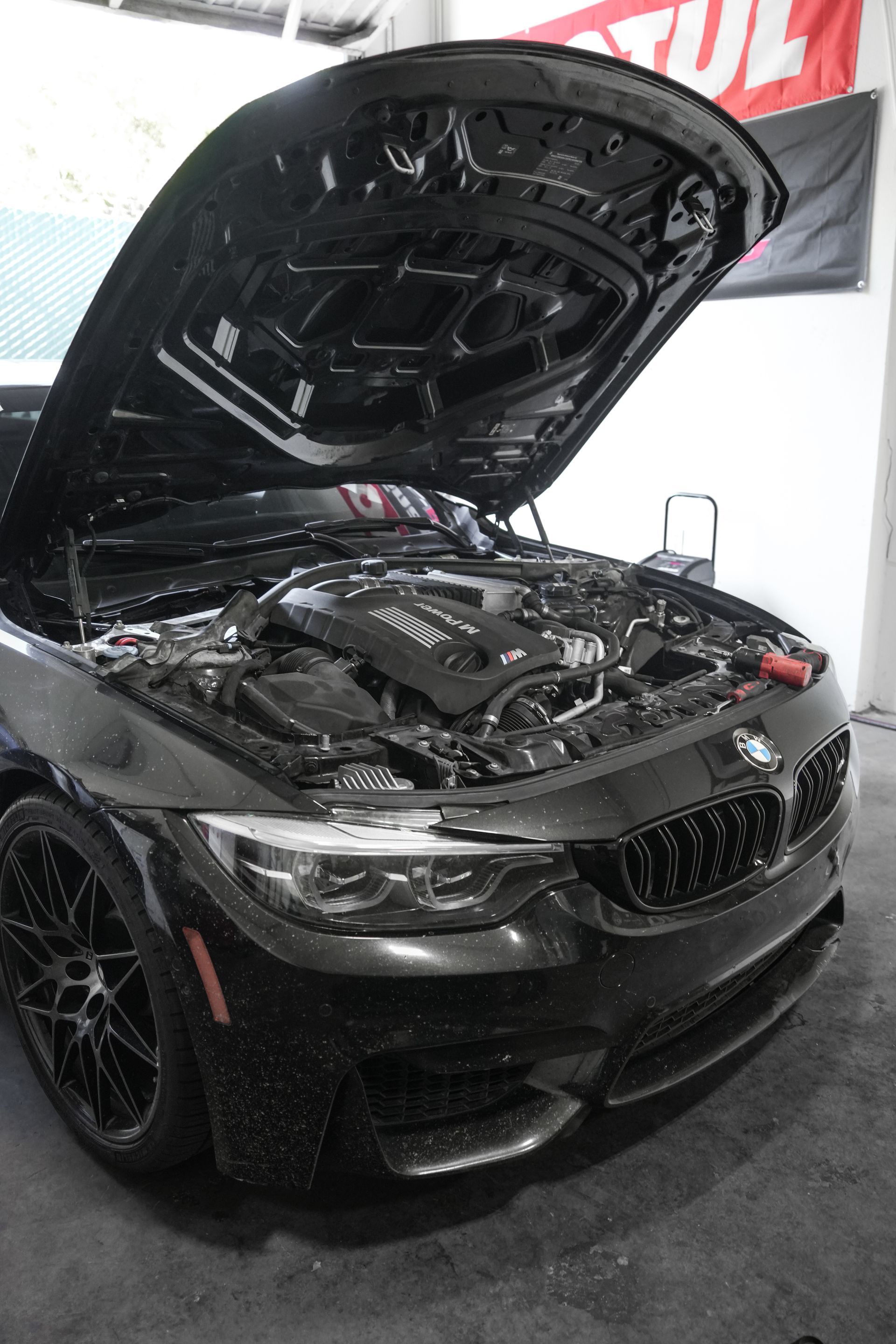 Black BMW sports car with hood open at an indoor auto show booth
