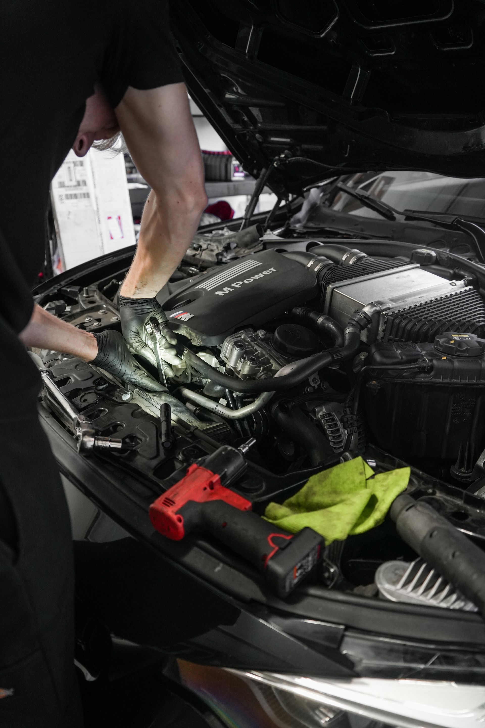 Person working on a car engine with the hood open, using tools in a garage.
