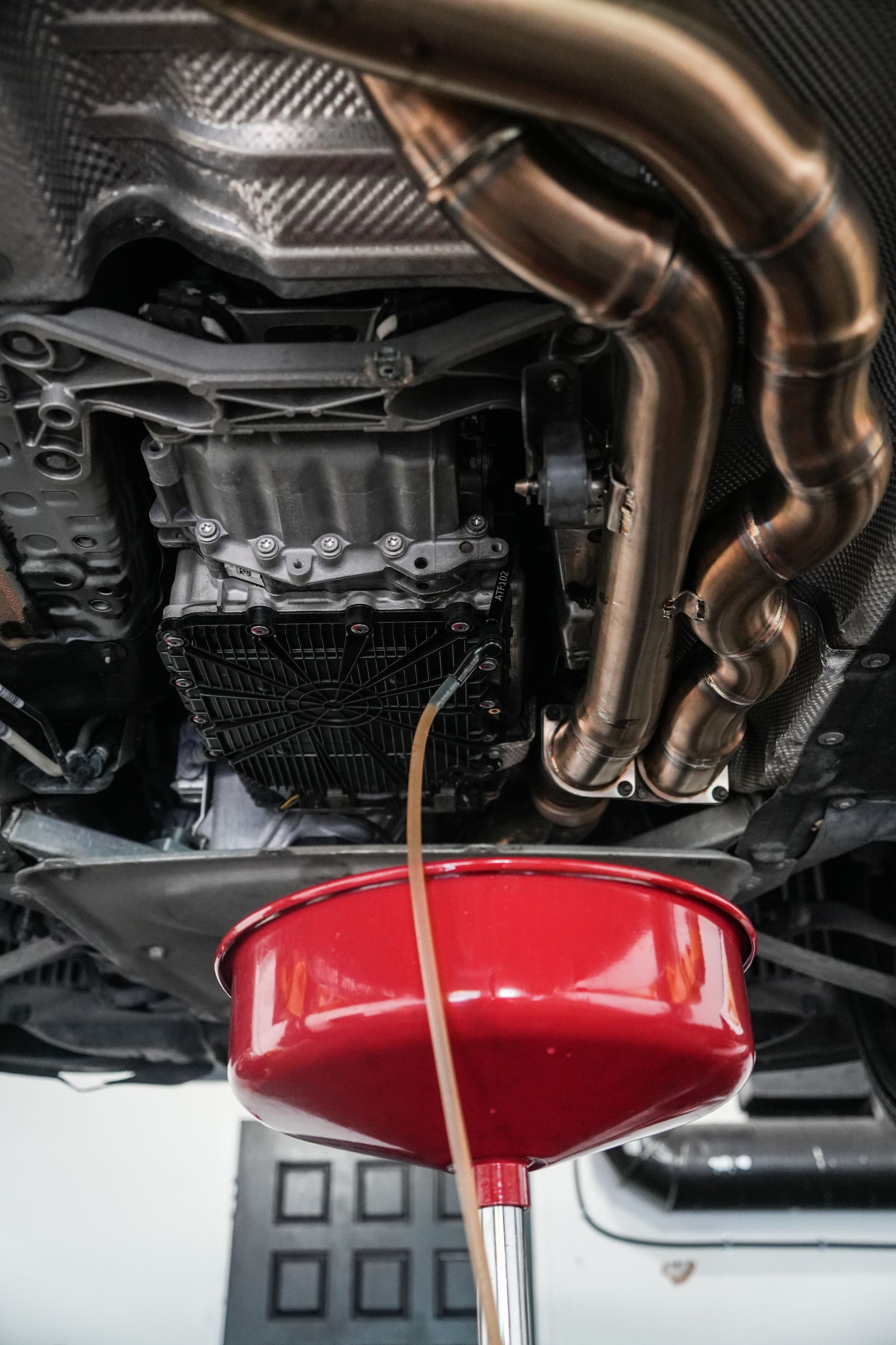 Red oil drain pan catching fluid under a car on a lift in a garage