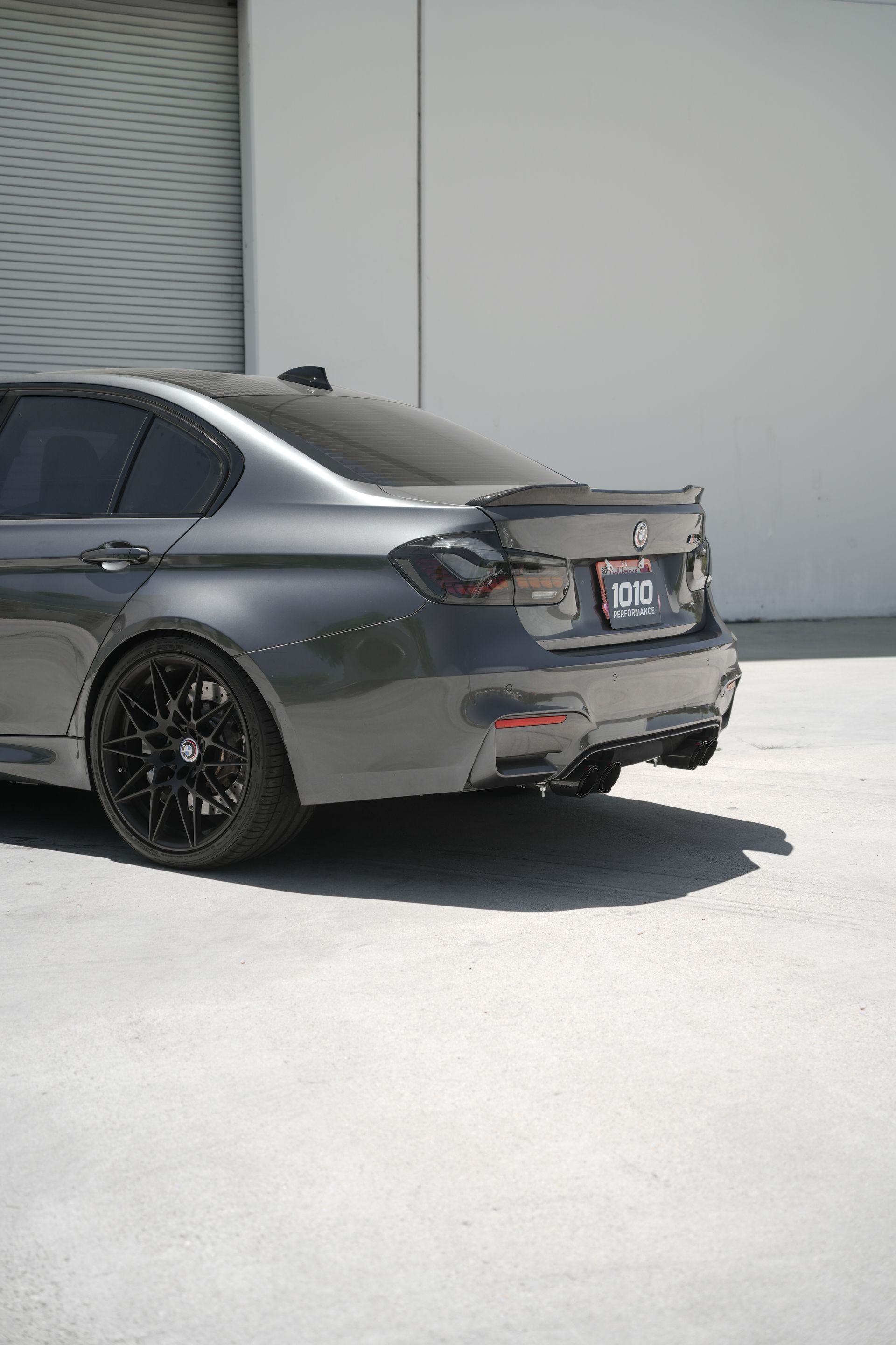 Gray sedan parked beside a warehouse wall in bright sunlight.