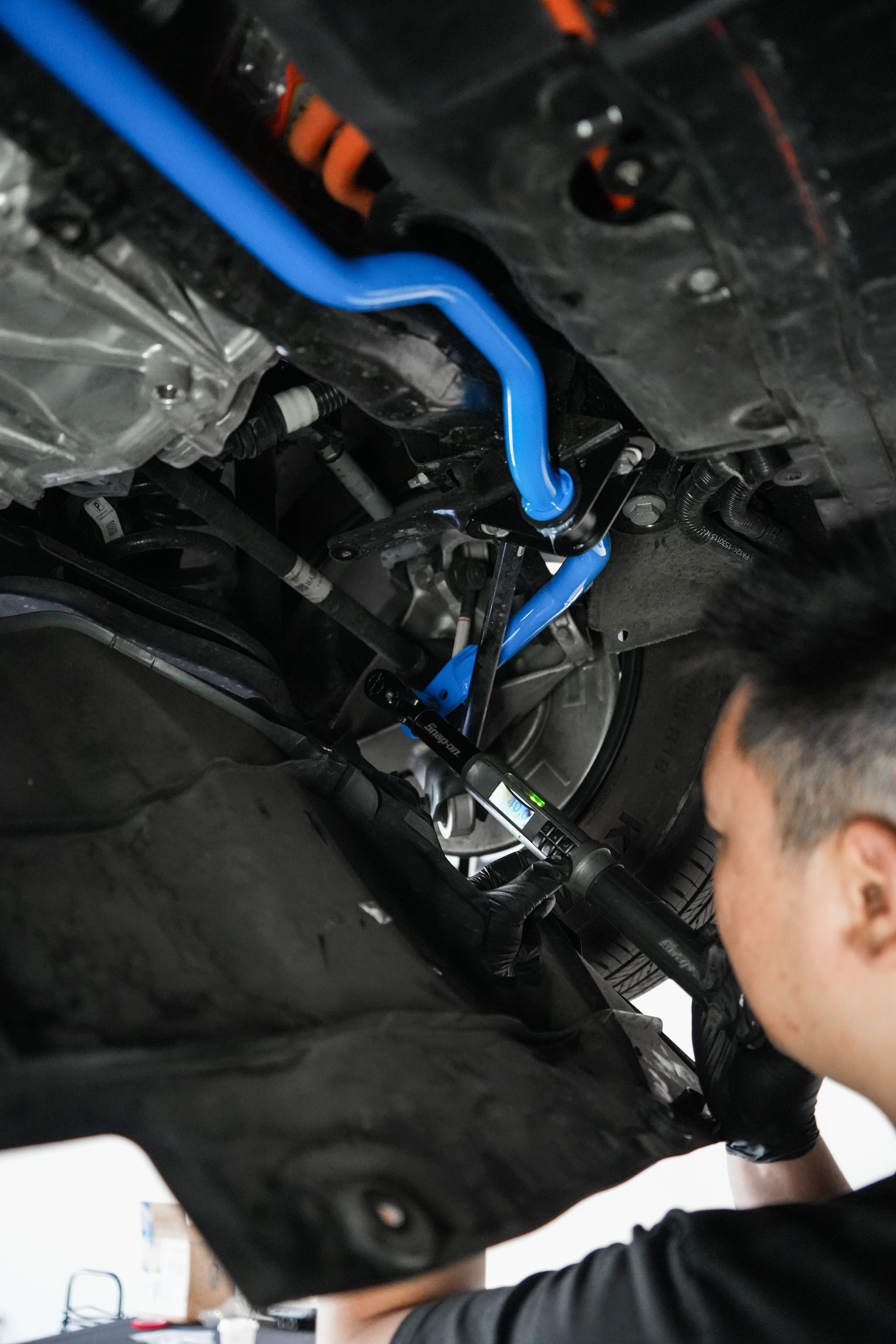 Mechanic inspecting blue hoses and wiring under a vehicle dashboard