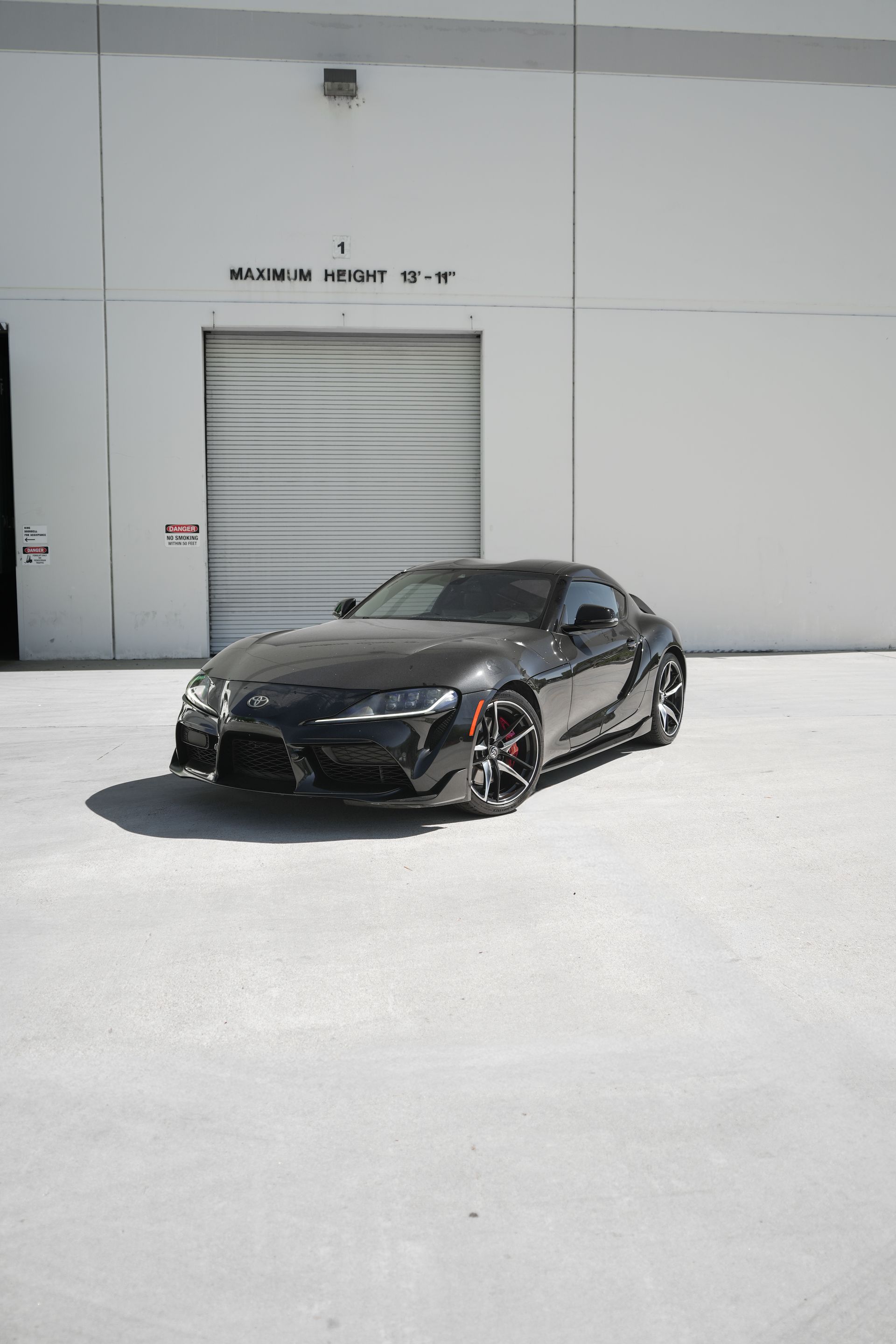 Black sports car parked in front of a white warehouse door on a bright day