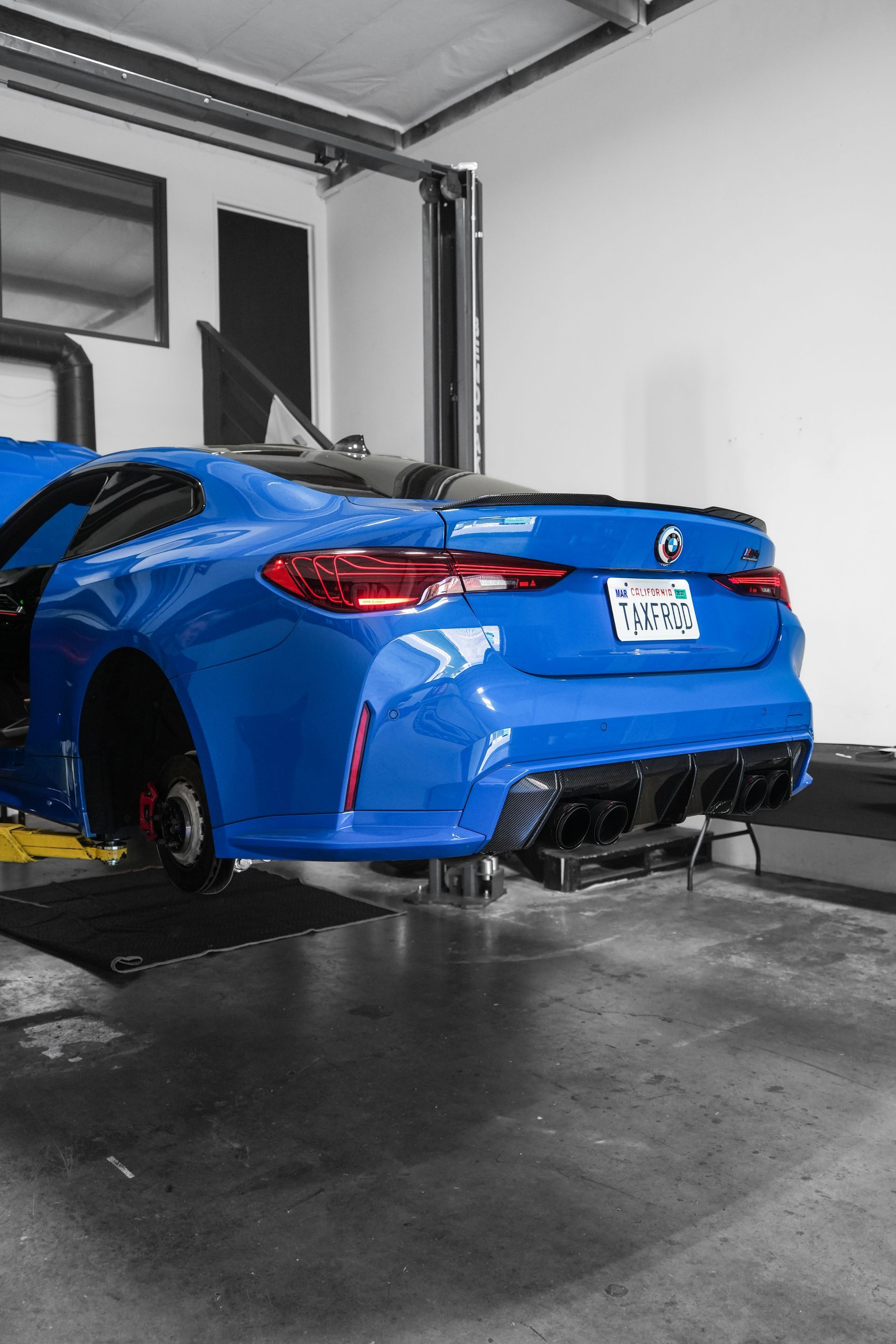 Blue sports car on a lift in a garage, rear view with a white license plate.