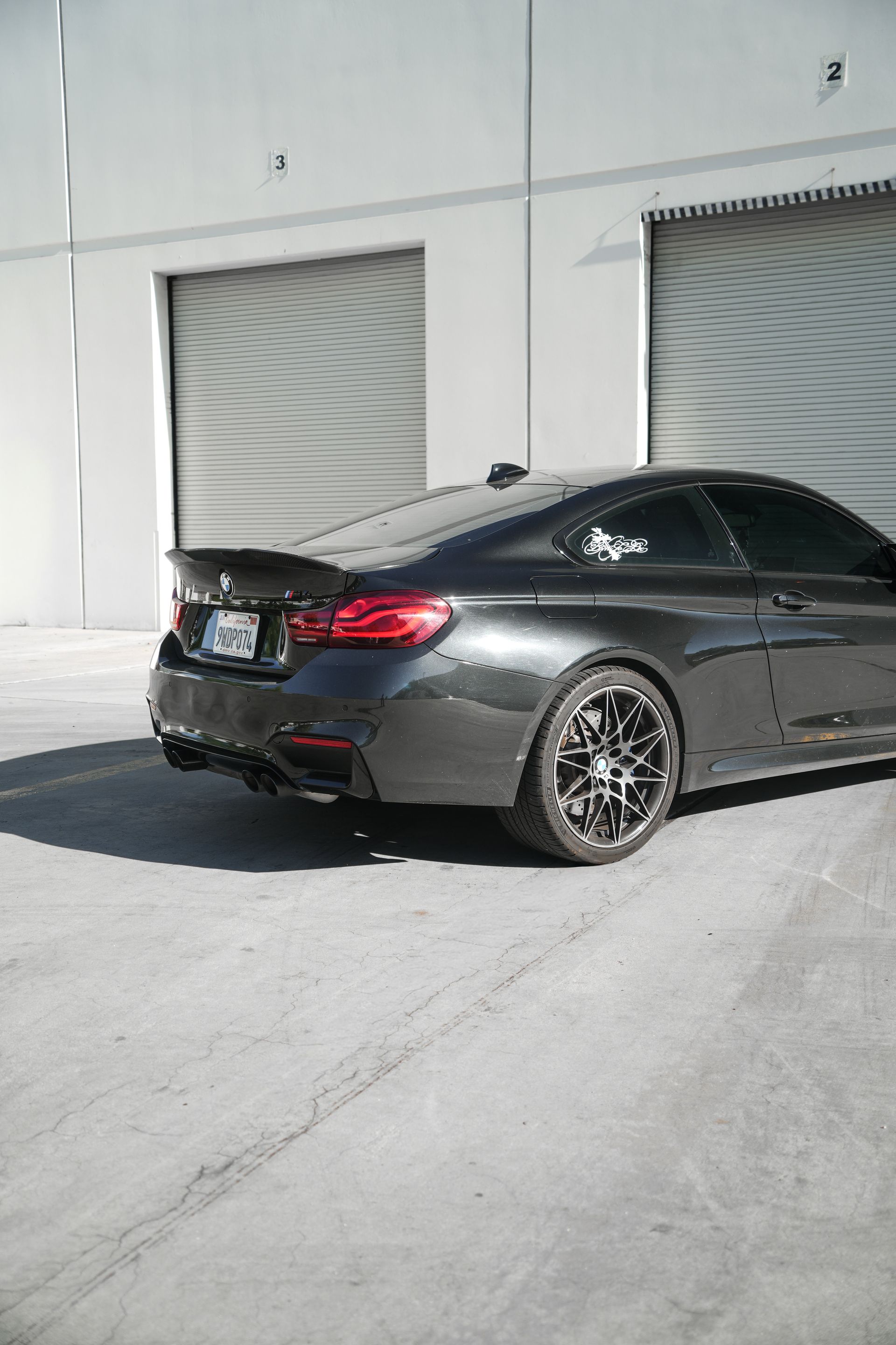 Black coupe parked outside a white industrial building with roll-up doors