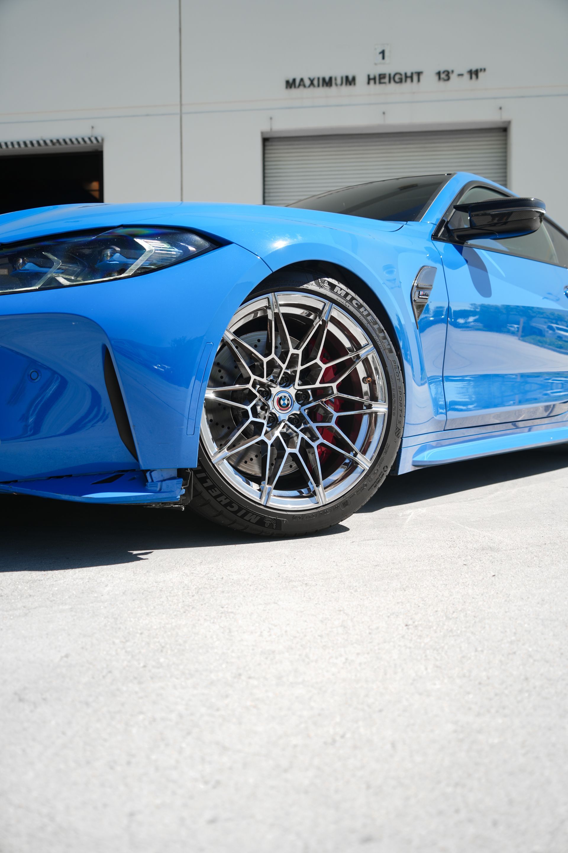 Blue sports car parked outside a garage, showing front wheel and side profile.