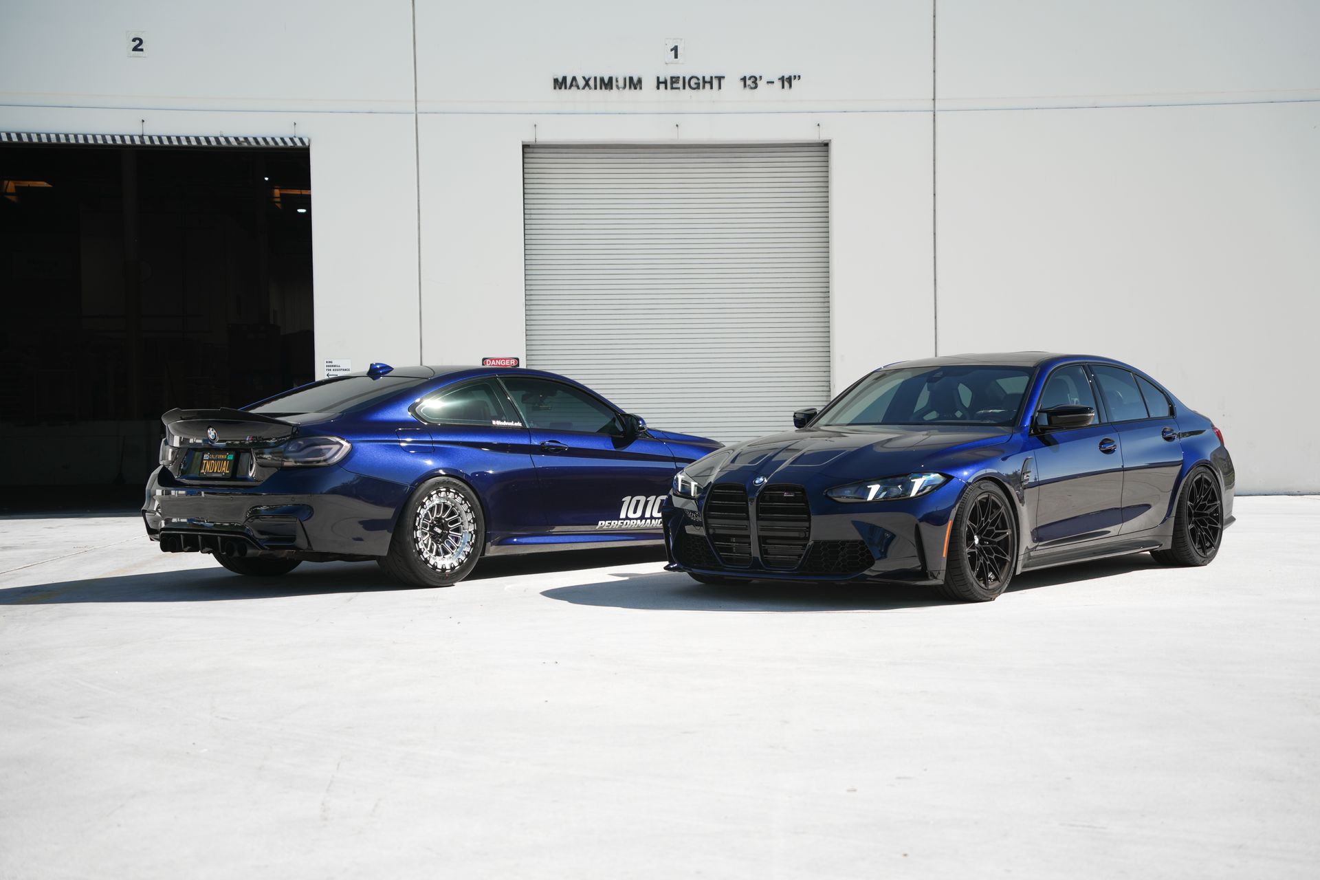 Two blue sports sedans parked side by side outside a white building
