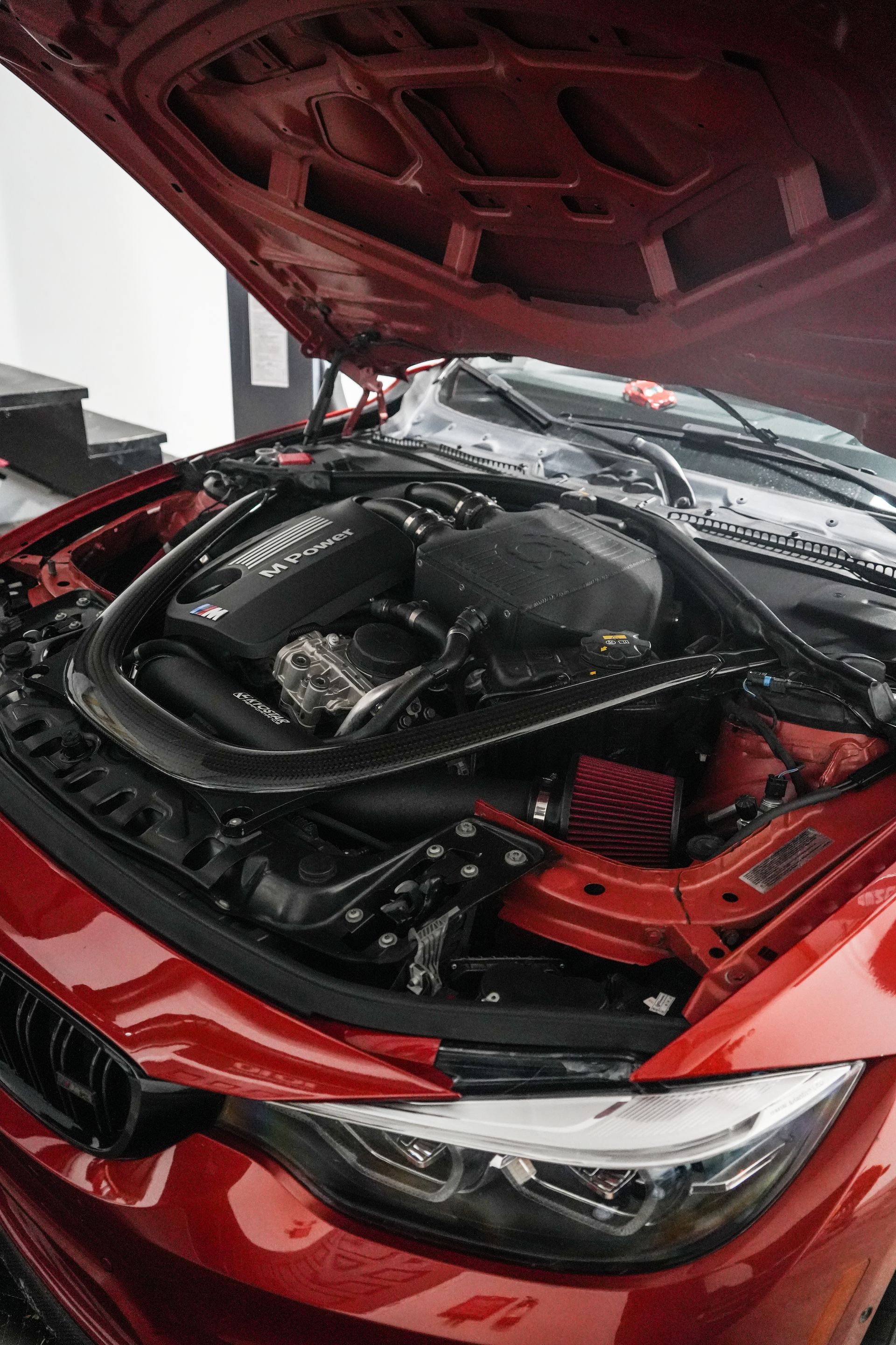 Red car with hood open, showing the engine bay in a close-up view.