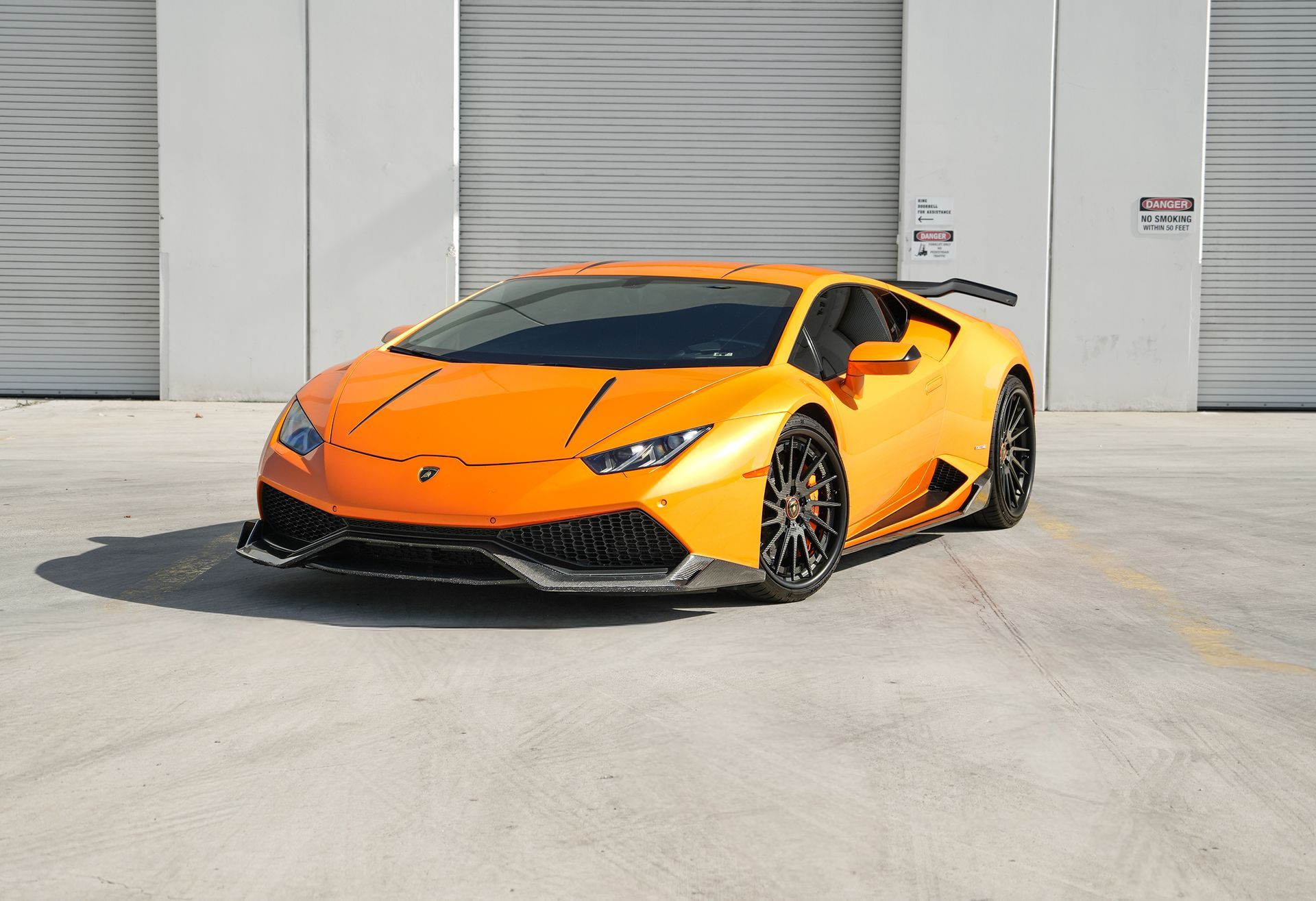Orange sports car parked in front of gray warehouse doors.