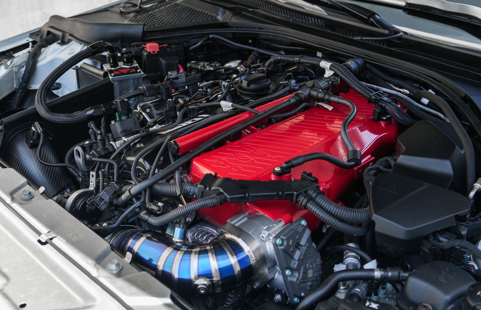 Car engine bay with a bright red engine cover and blue-striped intake piping.