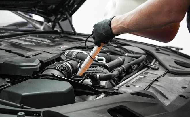 Mechanic using a dipstick to check engine oil in a car’s open hood engine bay