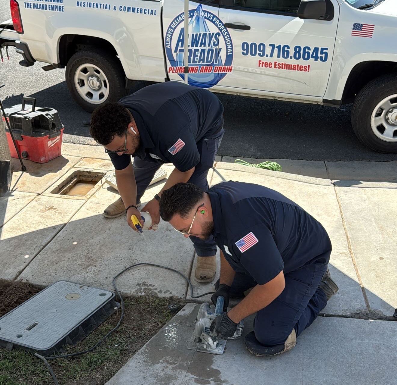 Two workers in navy shirts repair concrete, near a white truck with logo