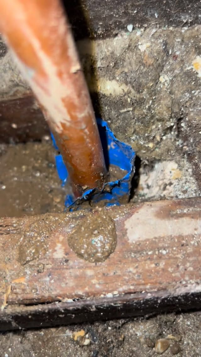 Close-up of a copper pipe with blue plastic, in a dark, dirty setting.