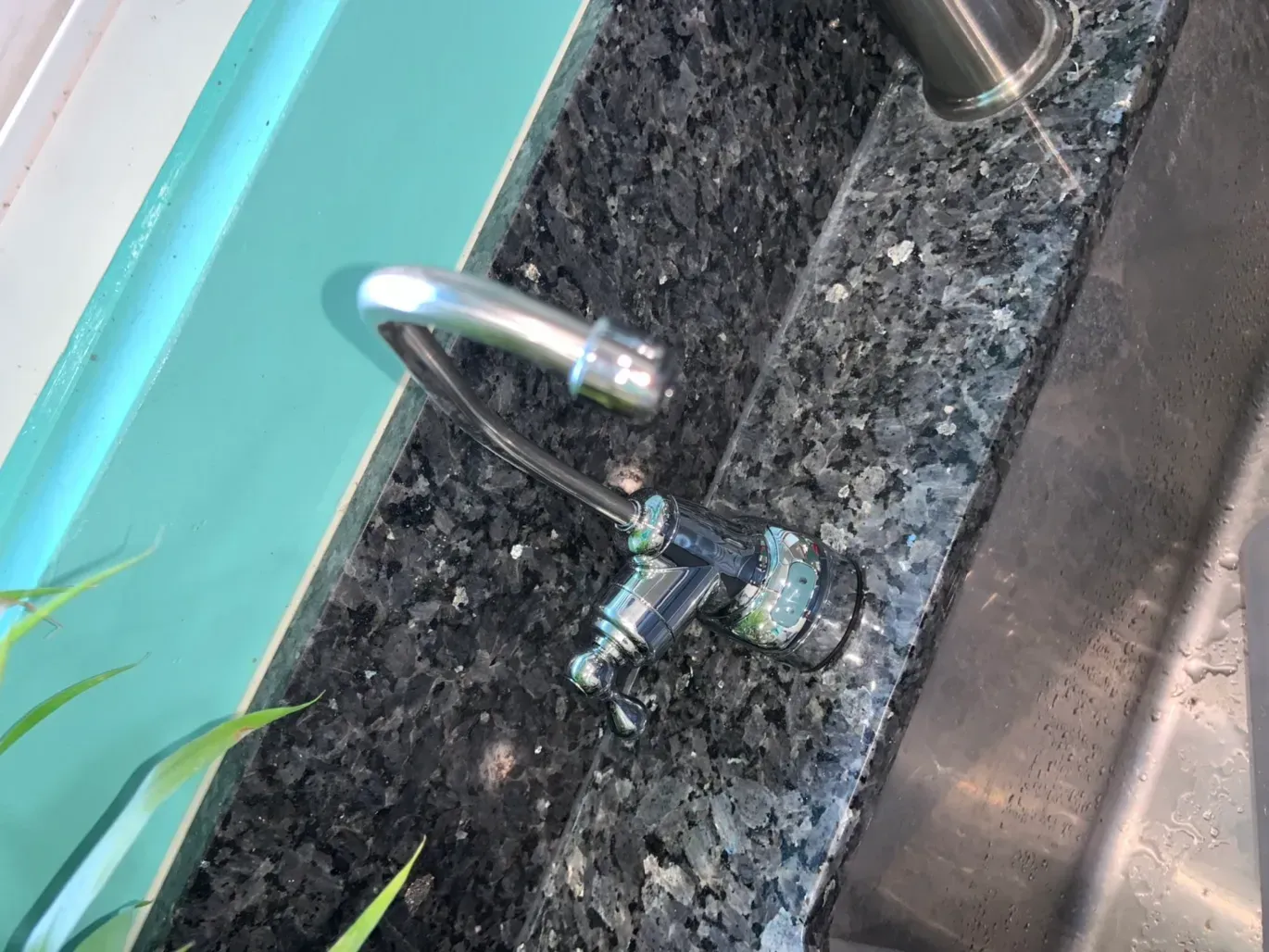 Chrome faucet on black speckled countertop, adjacent to a teal-painted surface and a stainless steel sink.