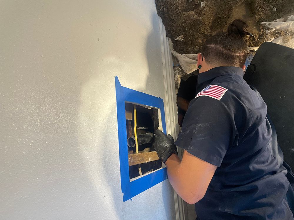 A person wearing a dark blue uniform inspects an opening in a wall, using gloves.