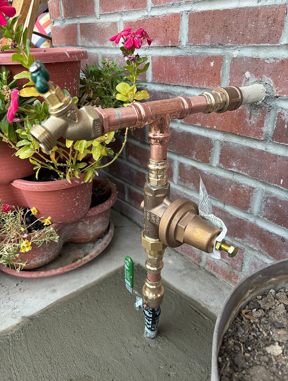 Copper and brass water pipe assembly attached to a brick wall. A green-handled valve is visible.