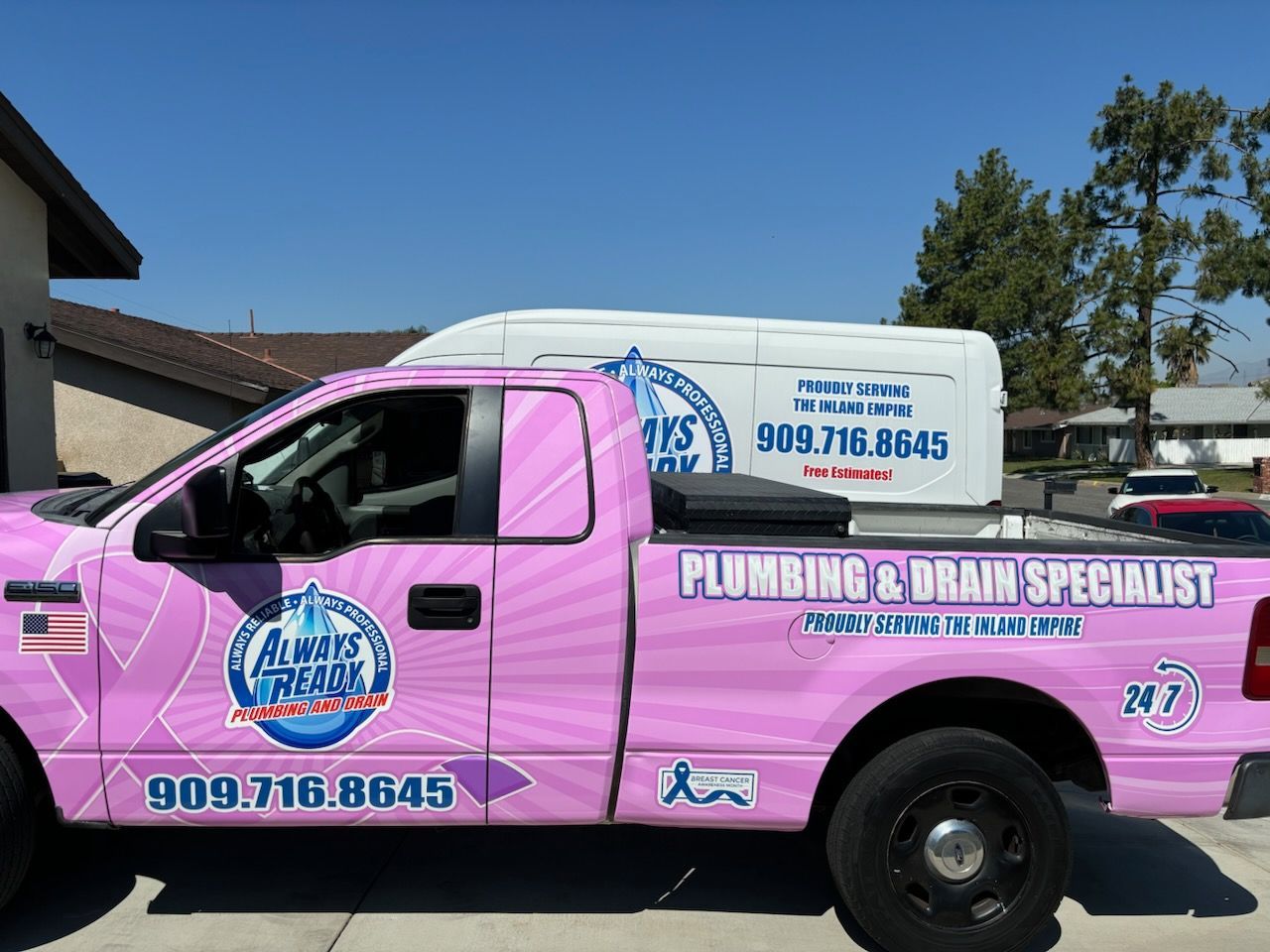Pink plumbing truck and van with company logo parked outside a building on a sunny day.