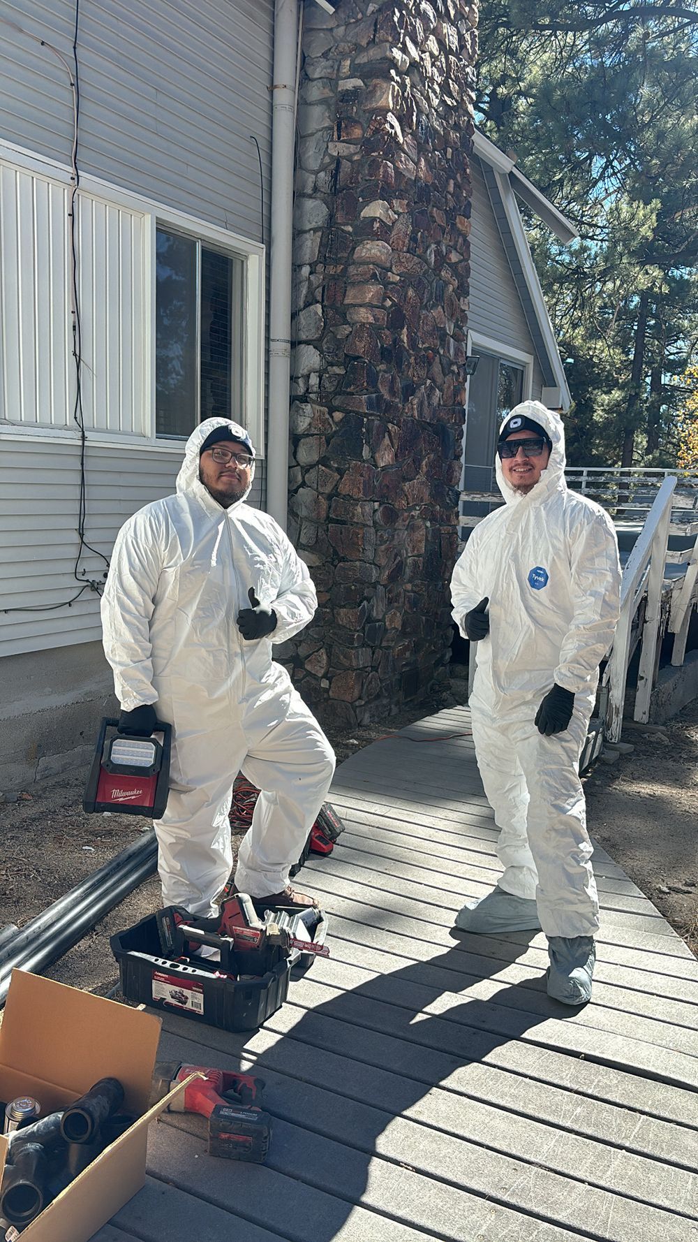 Two people in white coveralls pose next to a chimney and tools.