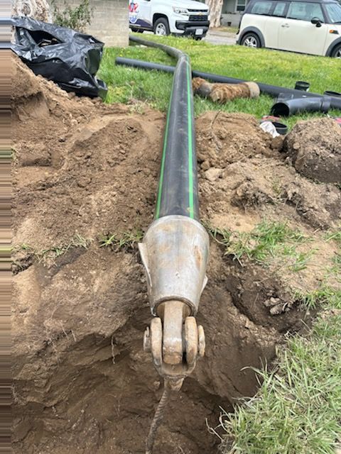 A long black pipe emerging from an excavated trench, connected to a metal joint.