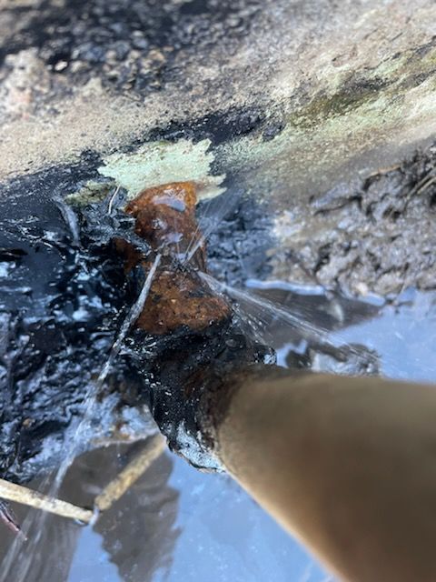Water spraying from a corroded metal pipe in a muddy environment.