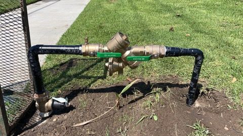 Irrigation system backflow preventer with green-handled valves and black pipes, in a grassy yard.