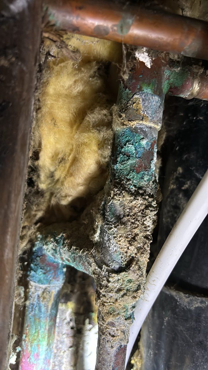 Corroded copper pipes with green and white buildup, surrounded by insulation in a close-up view.