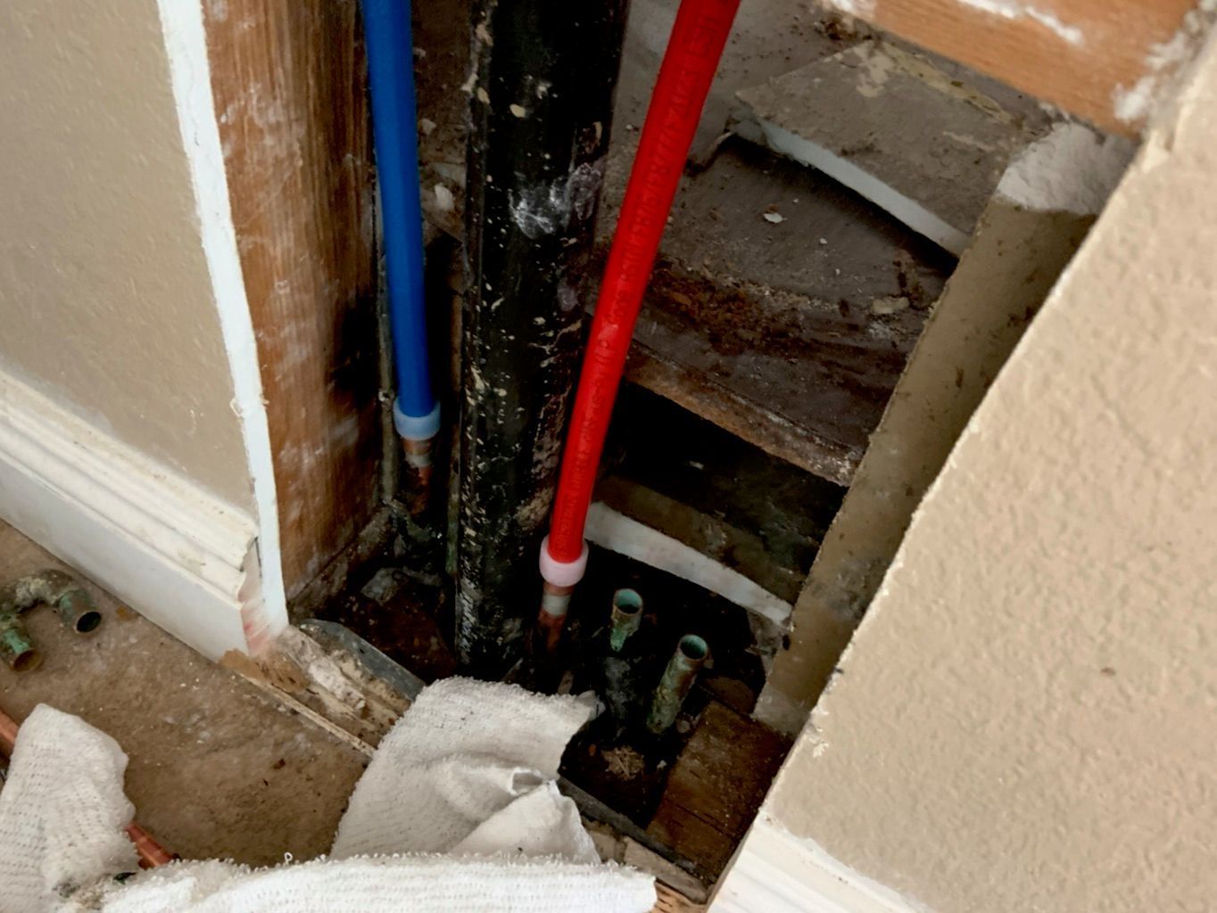 Plumbing pipes exposed in a wall opening; blue and red pipes visible alongside a black pipe; debris present.