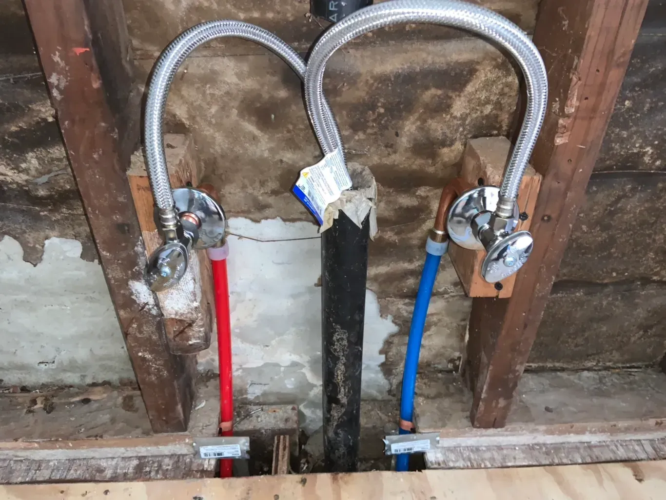 Pipes and valves in a wall. Red and blue water lines, metal flex lines connected to valves.