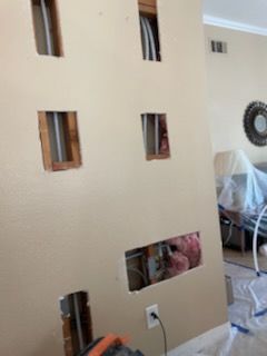 Wall with several rectangular holes exposing pipes and insulation. An electrical outlet is visible.