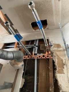 Plumbing repair in progress: flexible water lines, exposed pipes, and a damaged ceiling.