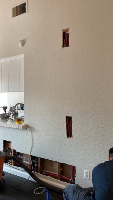 Interior wall with electrical boxes and exposed wiring; worker kneels.
