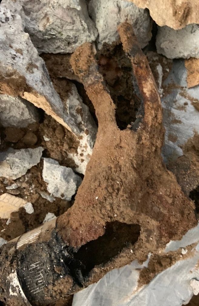 A corroded metal object, possibly a handle or support, embedded in soil and rocks.