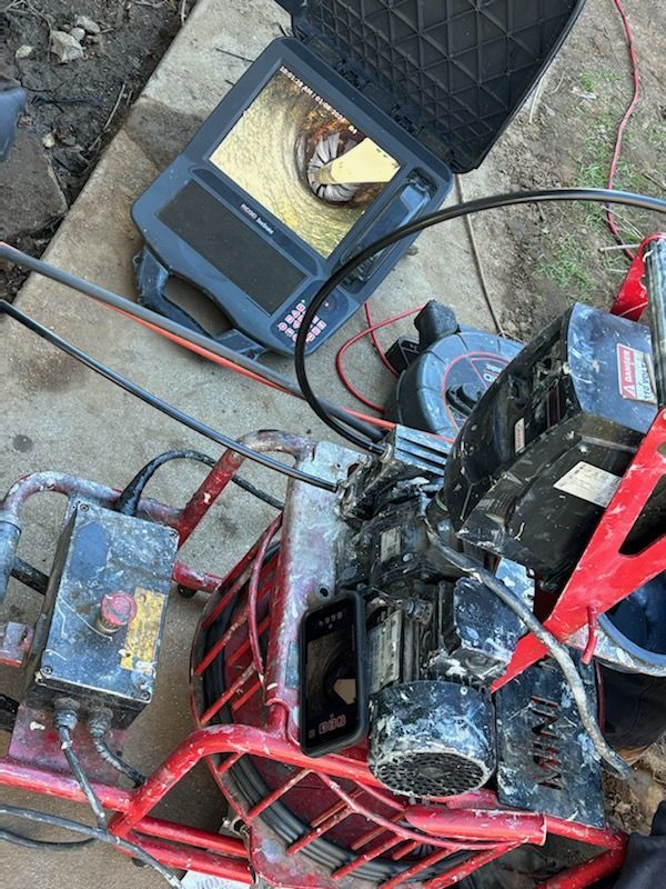 Inspection equipment, including a monitor showing a pipe interior, and a red machine, outdoors.