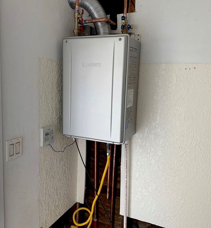 A wall-mounted tankless water heater with copper pipes, a flexible gas line, and a vent.