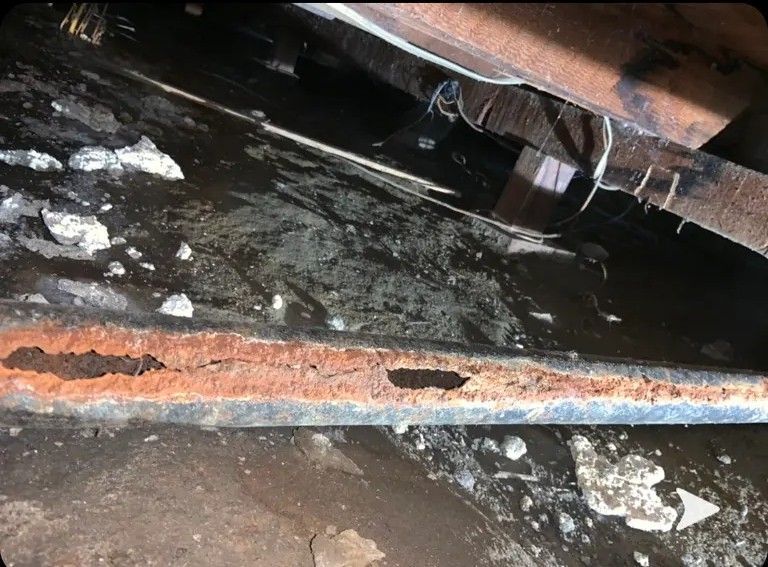 Heavily rusted metal pipe with visible holes, surrounded by dark water and debris.