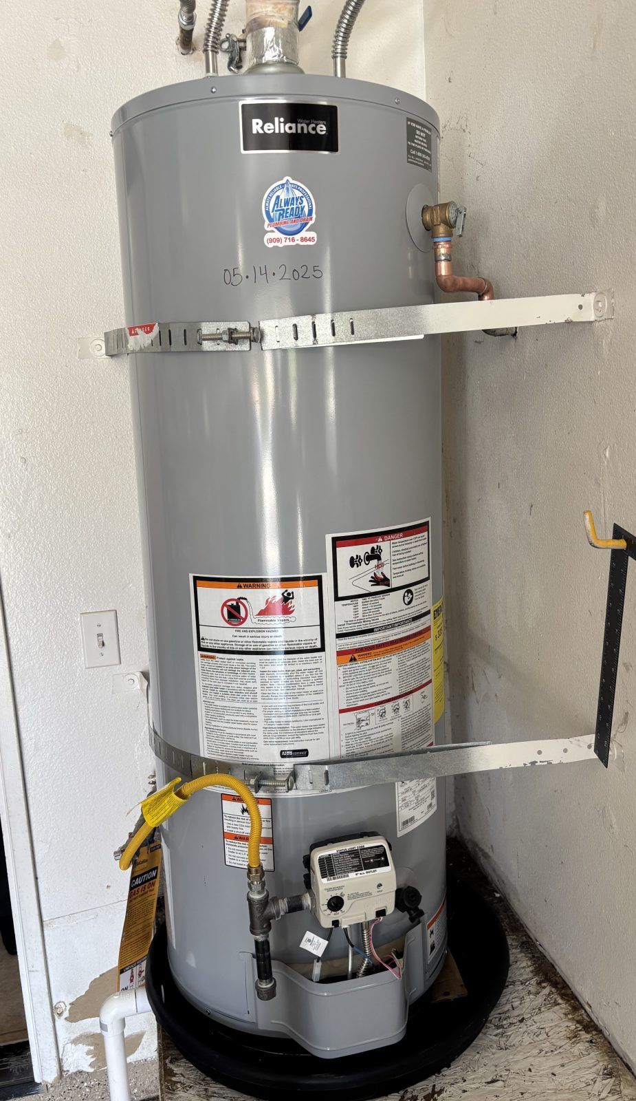 A tall gray water heater in a utility room. It has a gas line and various pipes.