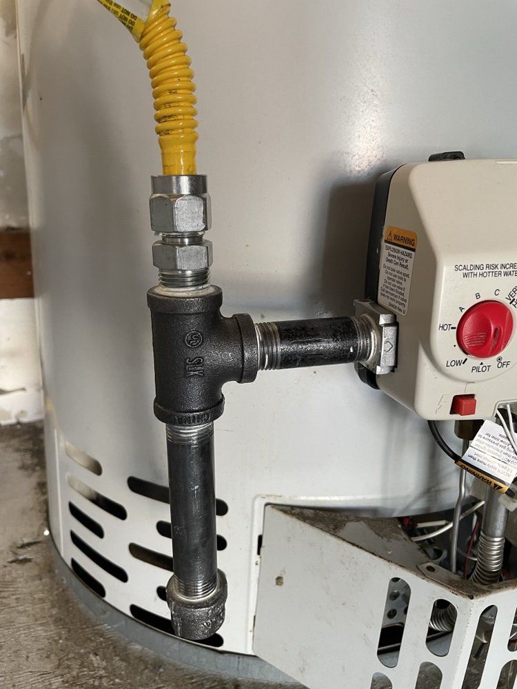 Gas line connection to a water heater, with yellow flexible tubing, black pipe fittings, and white appliance.