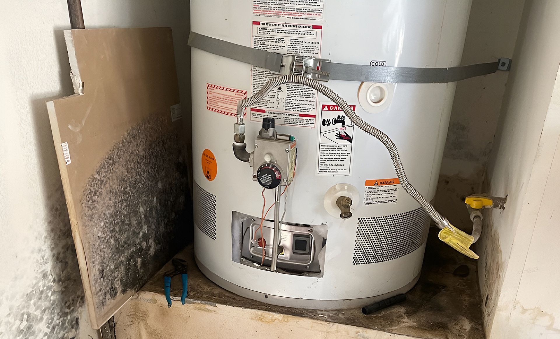 Water heater in a utility closet with mold growth on the surrounding walls.