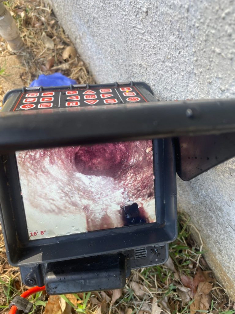 Black pipe connection exposed in a dirt trench; shadowed cavity behind.