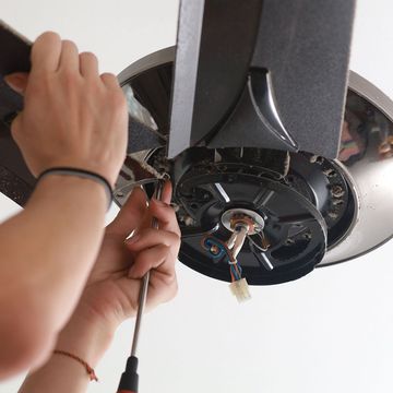 A person is fixing a ceiling fan with a screwdriver