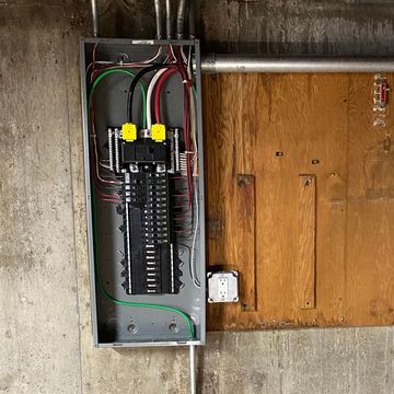 A electrical box is hanging on a wall next to a wooden door.