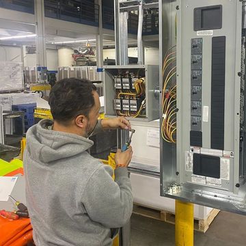A man is working on an electrical box in a warehouse