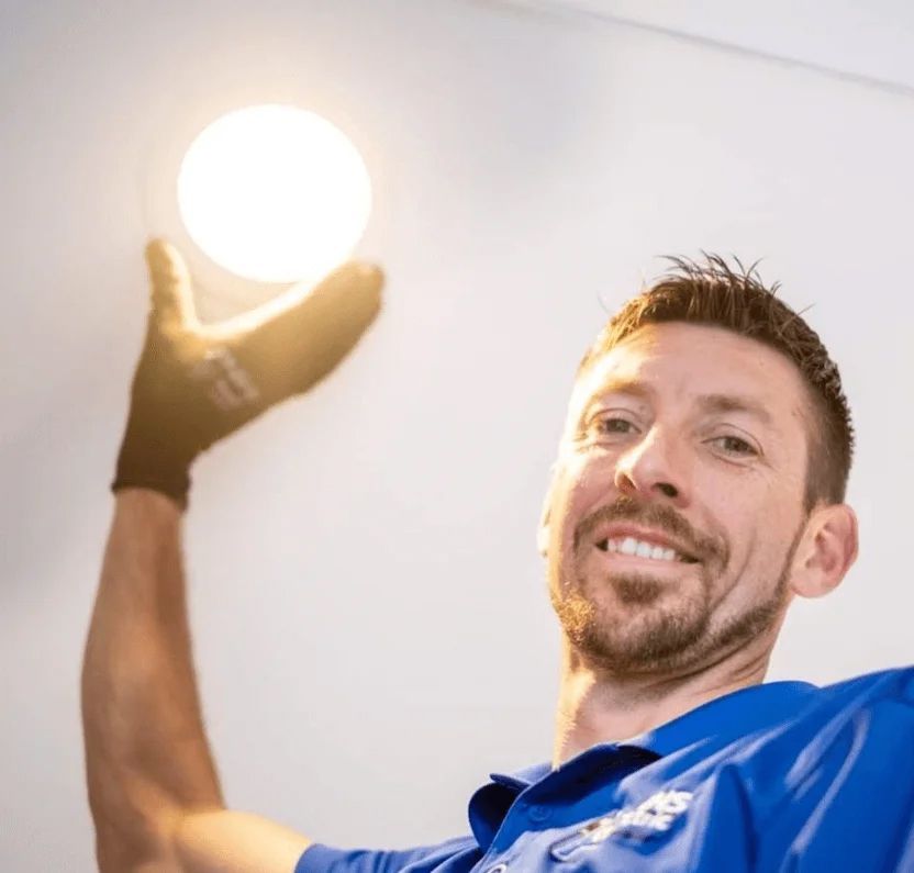 A man in a blue shirt is holding a light bulb in his hand.