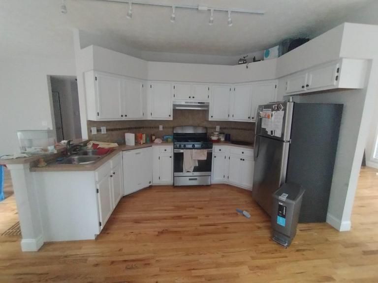 a kitchen with white cabinets , a stove , a refrigerator and a sink .