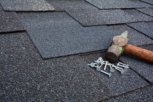 Hammer and nails on a gray shingled roof, with a roofing repair in progress.