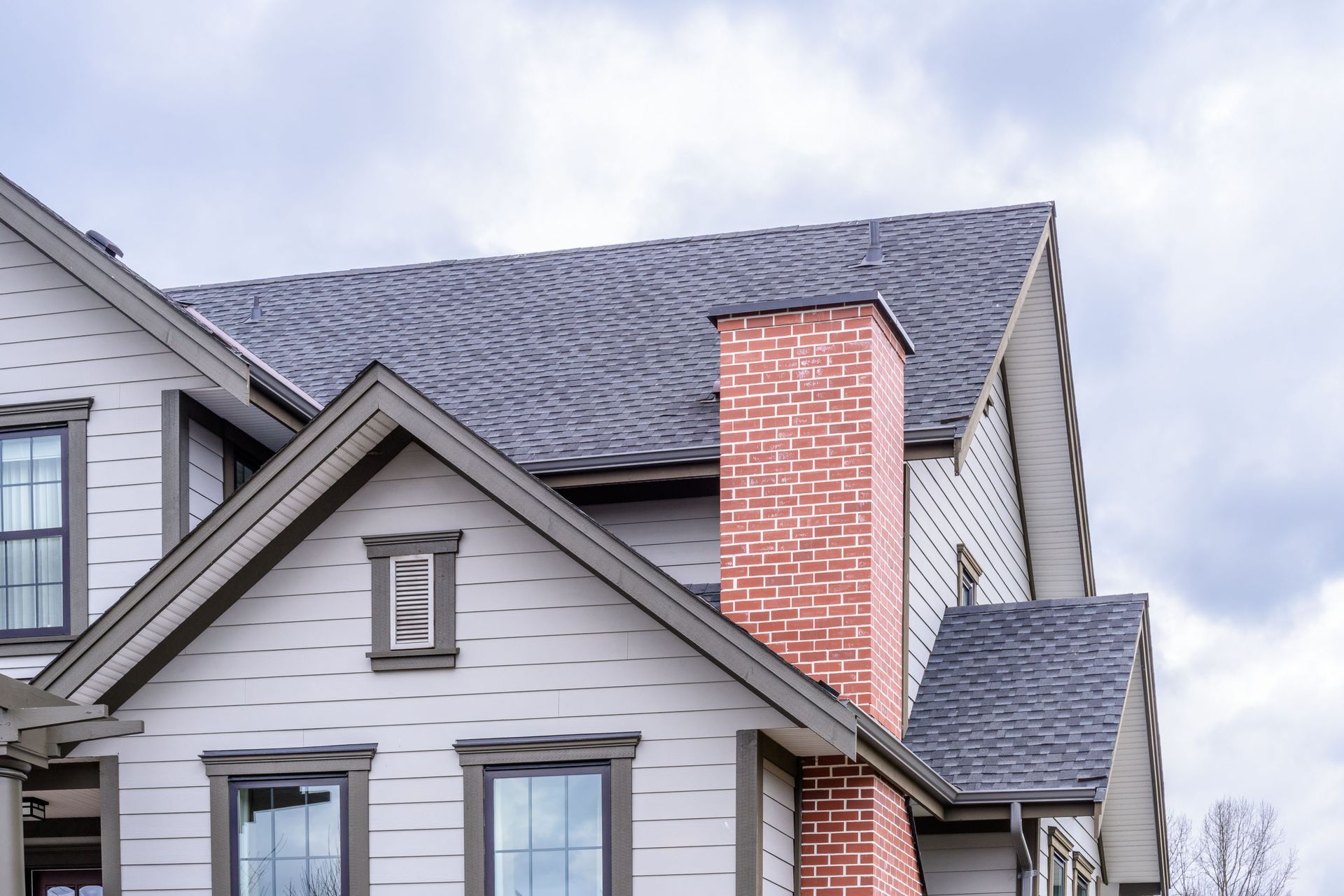Suburban house roof with gray siding and a red brick chimney under a cloudy sky