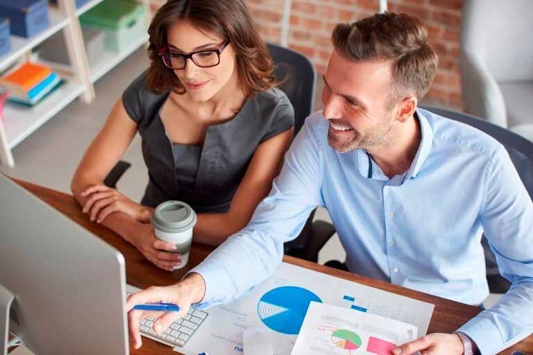 Woman and man looking at computer screen, reviewing data, smiling.