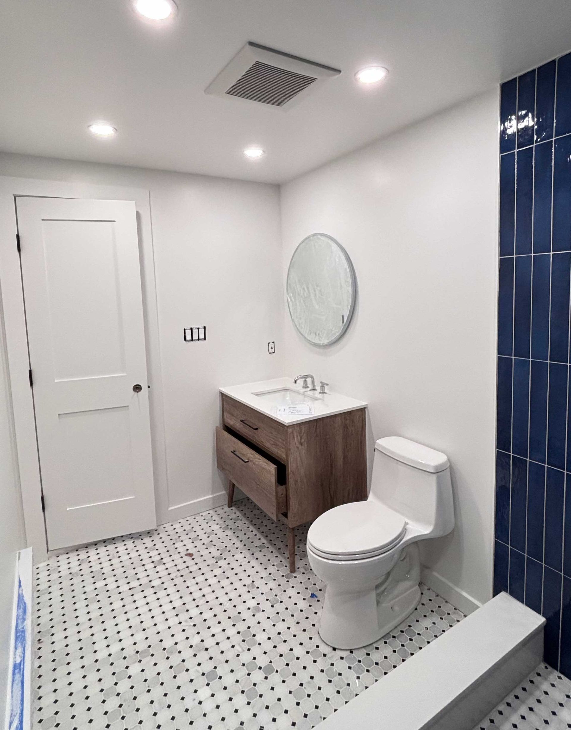 A newly renovated bathroom with white walls, a wooden vanity, and a blue tile accent wall.