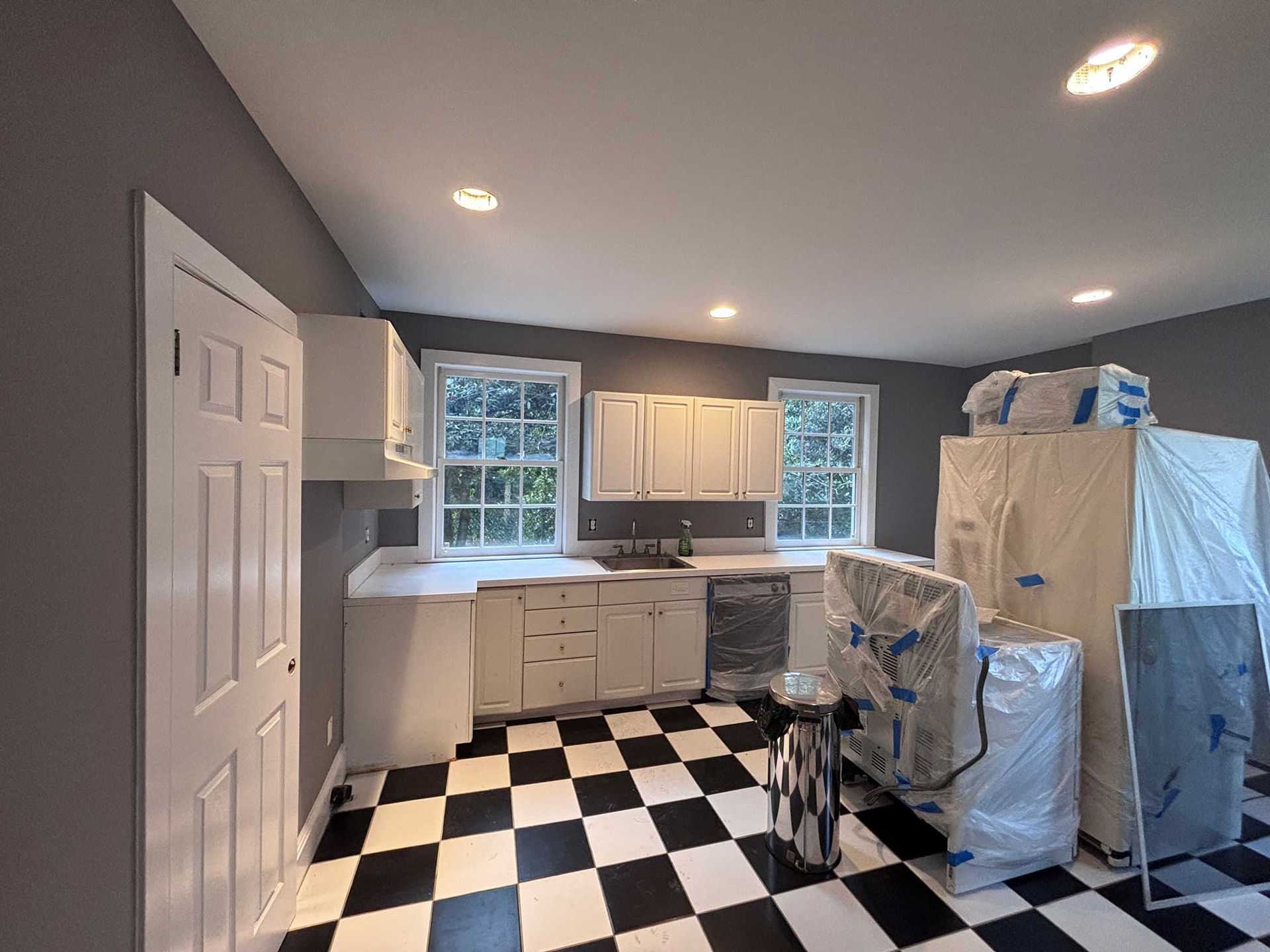 Kitchen with white cabinets, gray walls, black and white checkered floor, and windows.