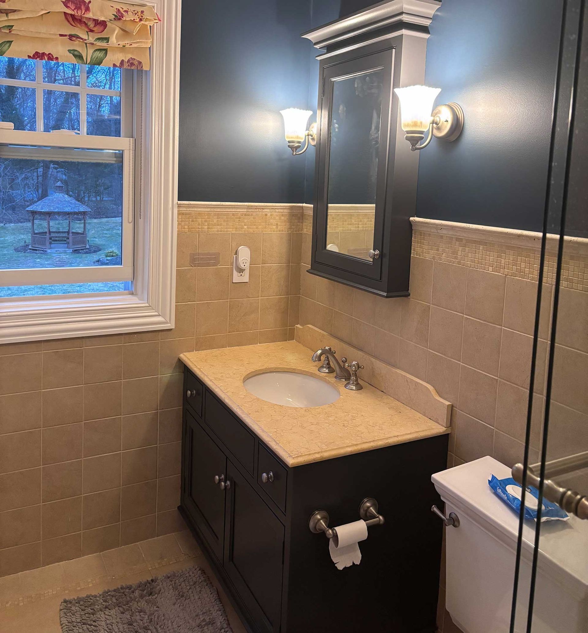 Small bathroom with dark vanity, beige tile, and a window with a view of a gazebo.